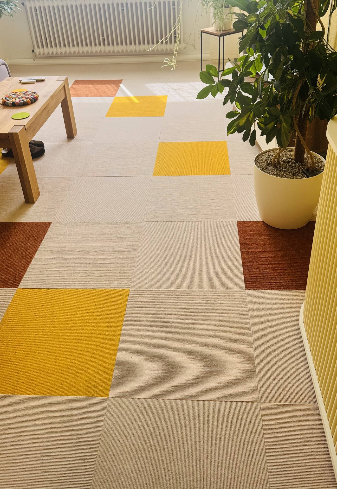 Teppichfliesen in Beige, Gelb und Rostrot als freies Muster in einem hellen Wohnraum