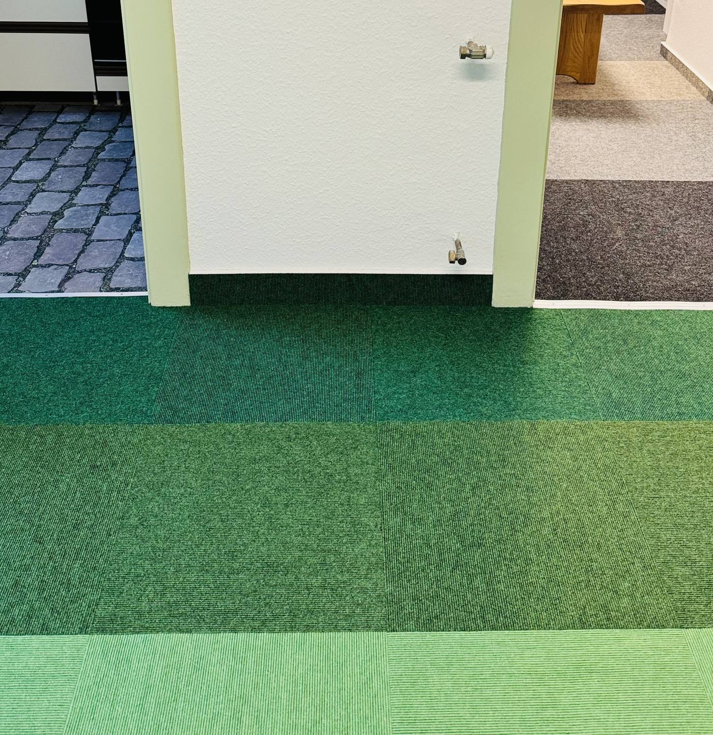Detail eines Bodenübergangs am Türdurchgang mit Teppichfliesen in grünen Farbabstufungen, verlegt in Dortmund