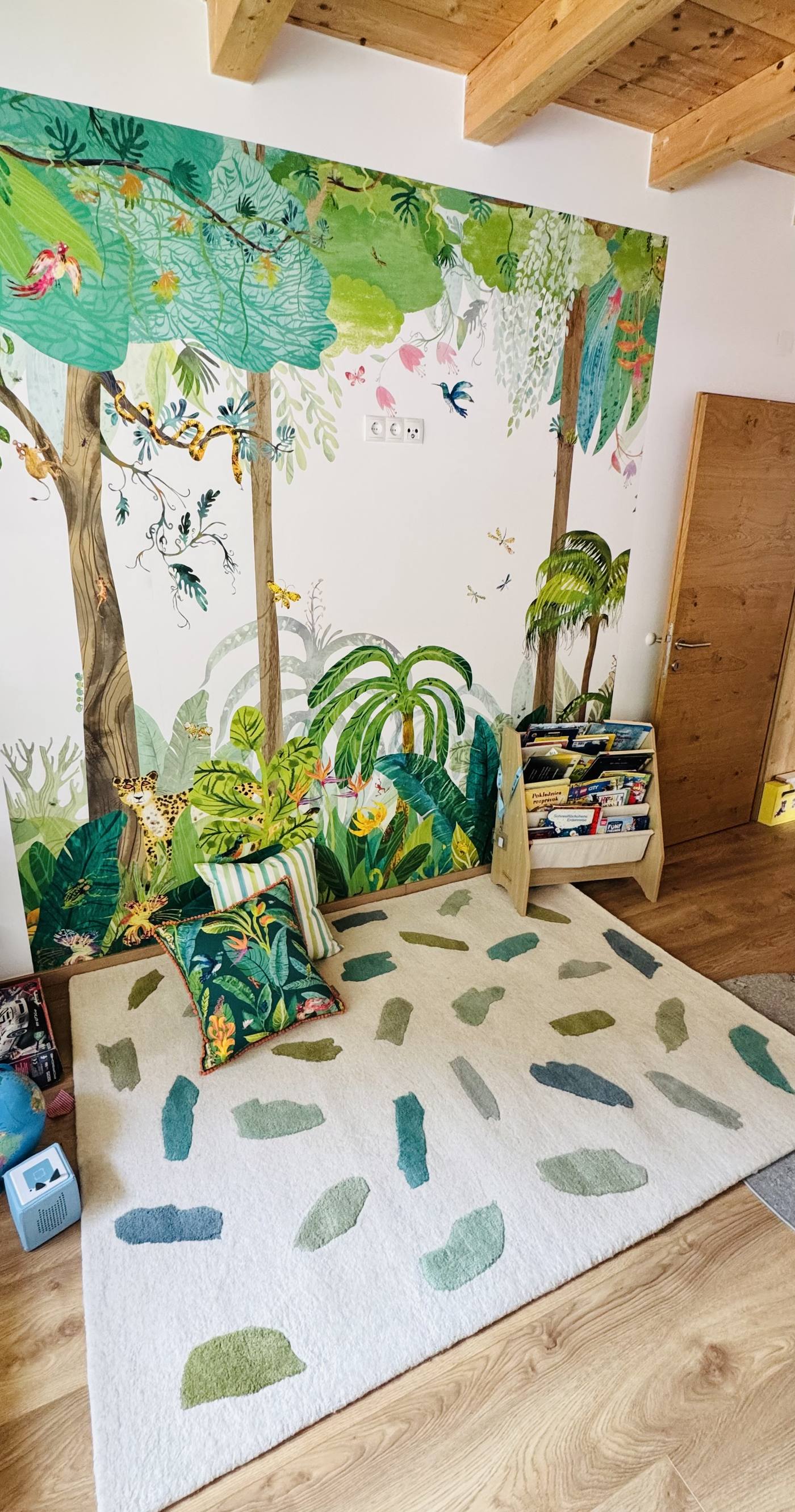 Kinderzimmer mit hellem Teppich mit grünen Farbtupfern vor einer Dschungel-Tapete
