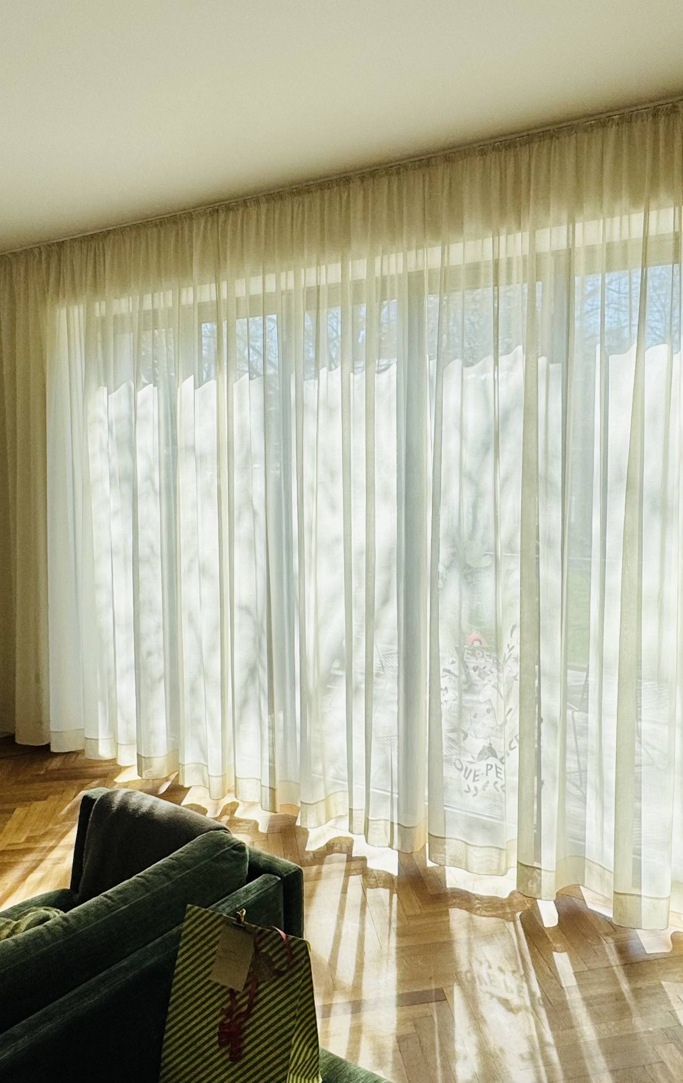 Sonnenlicht fällt durch einen raumhohen Store in ein Wohnzimmer