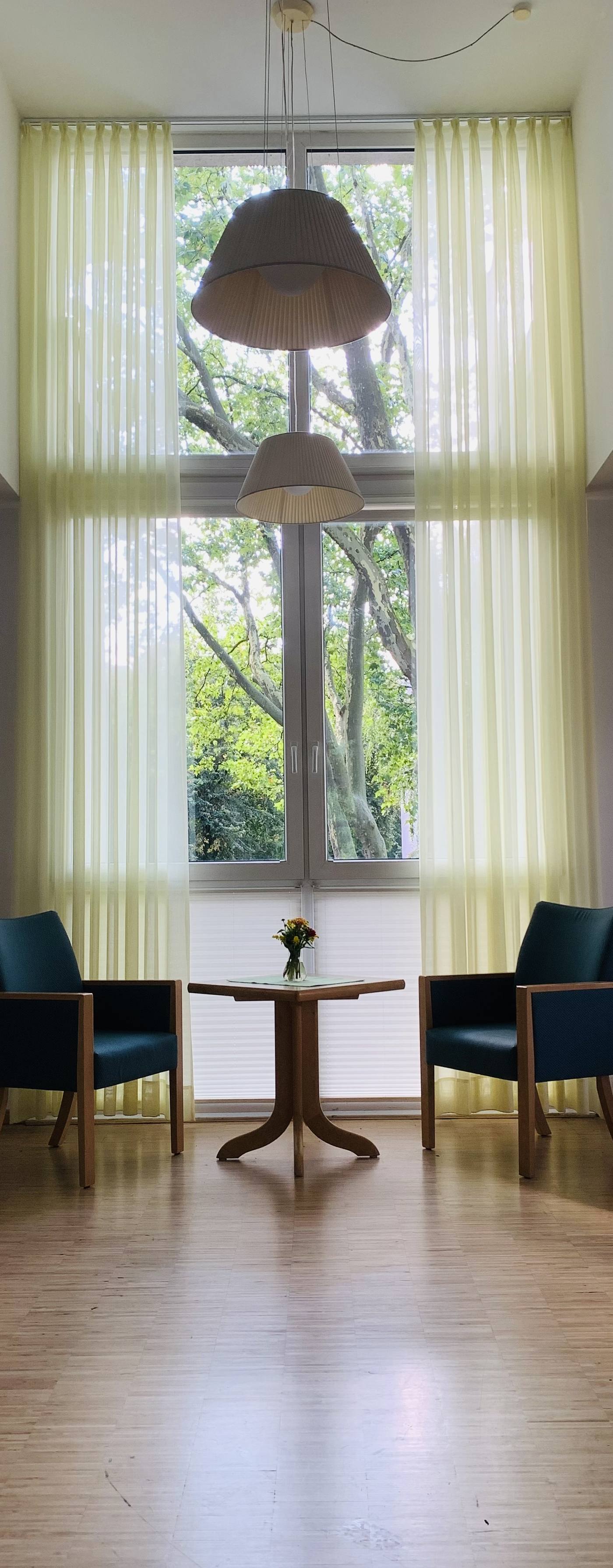 Raumhohe Stores an einem hohen Fenster mit Sitzgruppe davor