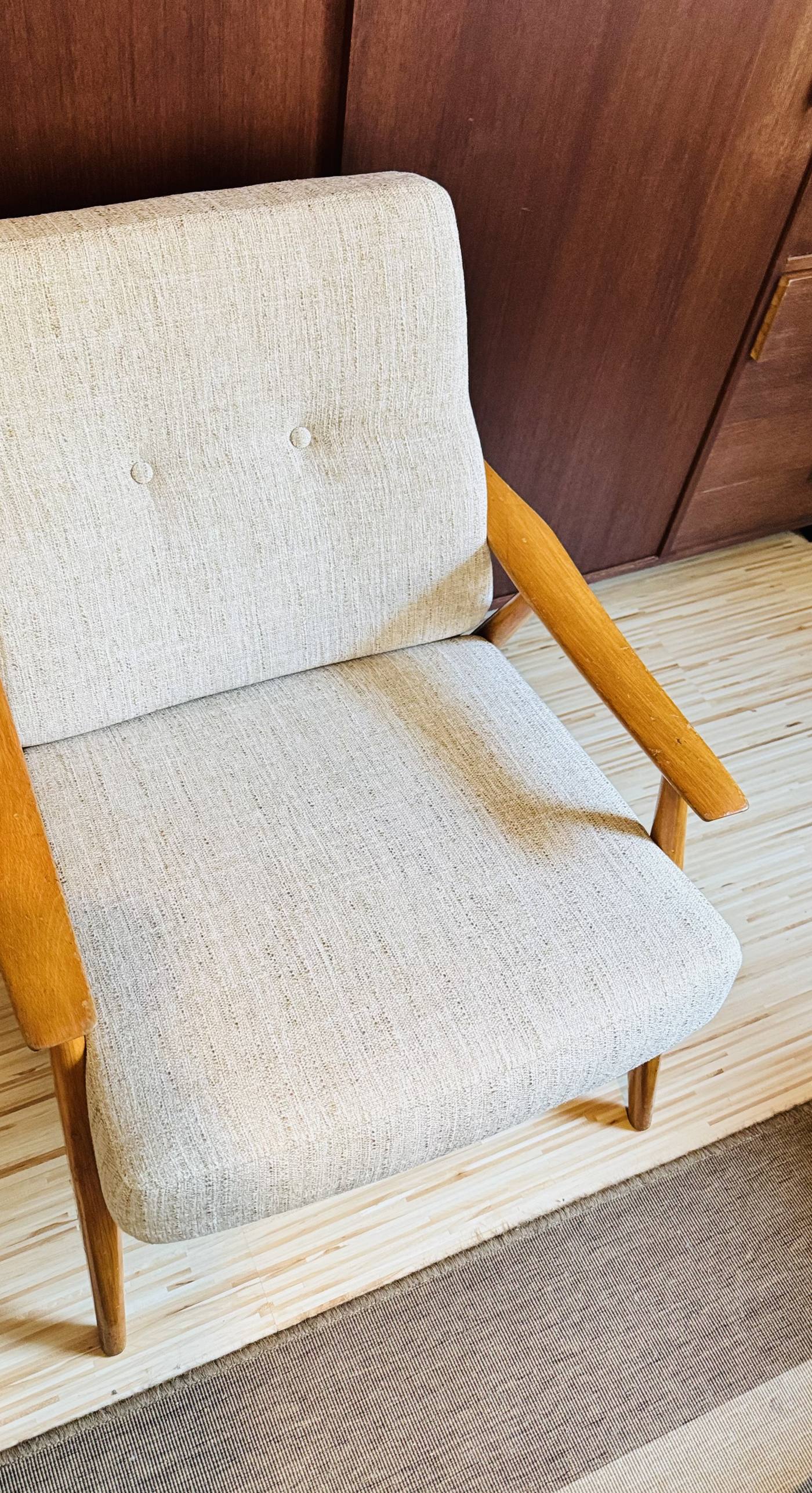 Sessel im Mid-Century-Stil mit cremefarbenem Bezug vor dunkler Holzwand